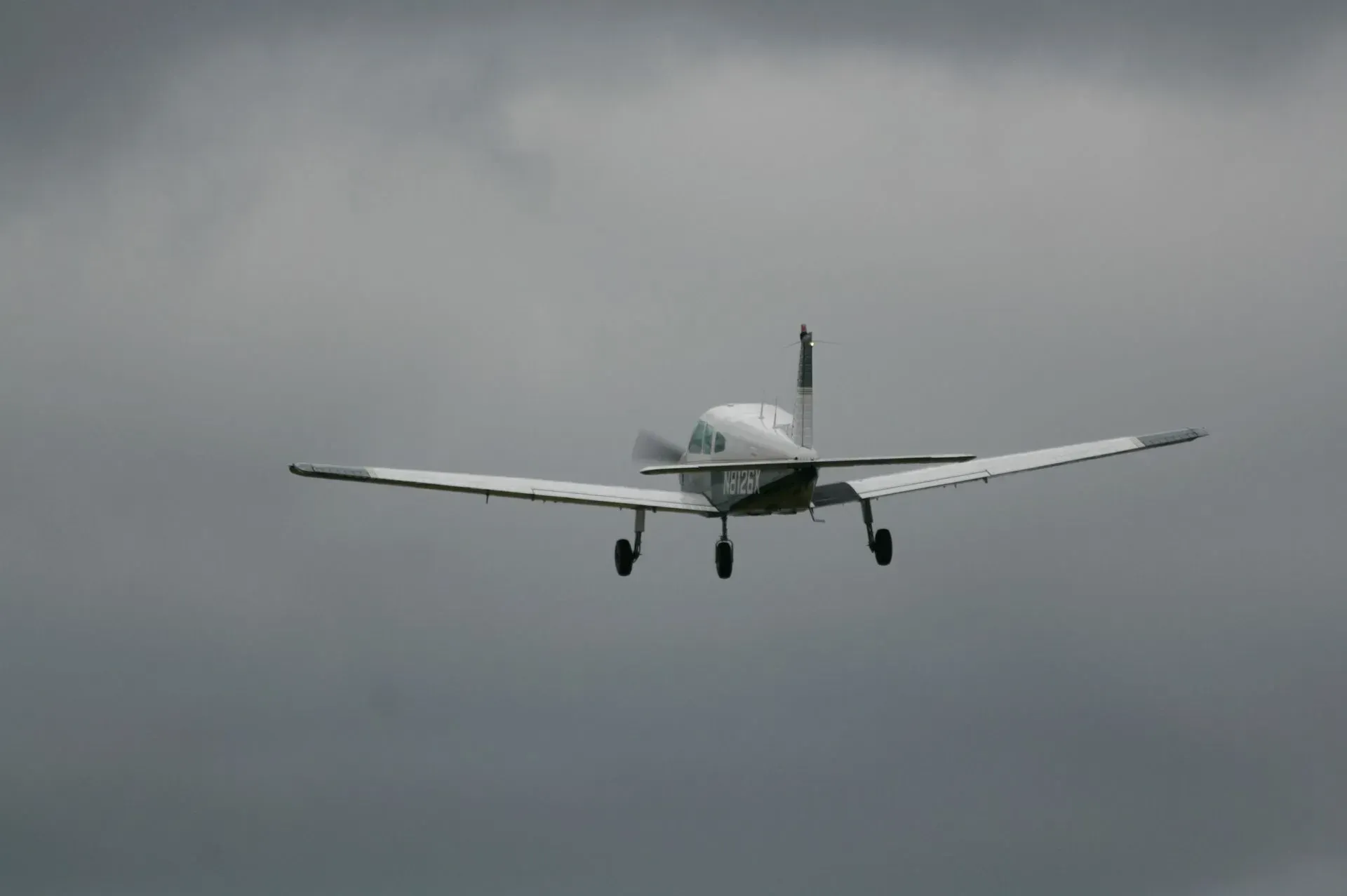 White airplane with landing gear down against a cloudy gray sky.
