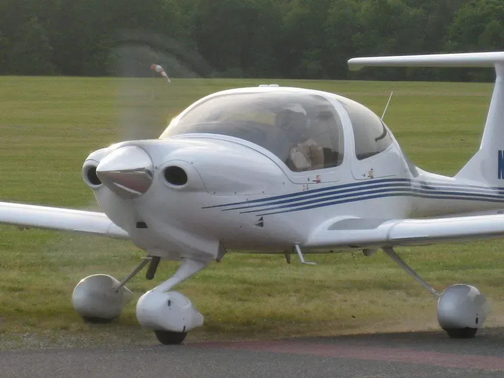 White airplane on a grassy field; blue stripes on the fuselage; nose propeller; clear glass cockpit.