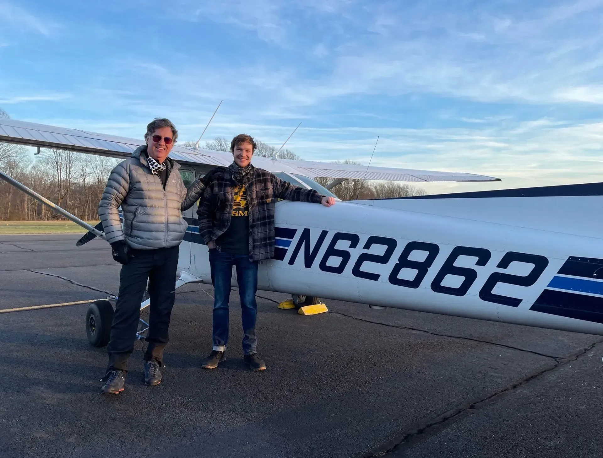 Two people stand next to an airplane on a tarmac; 