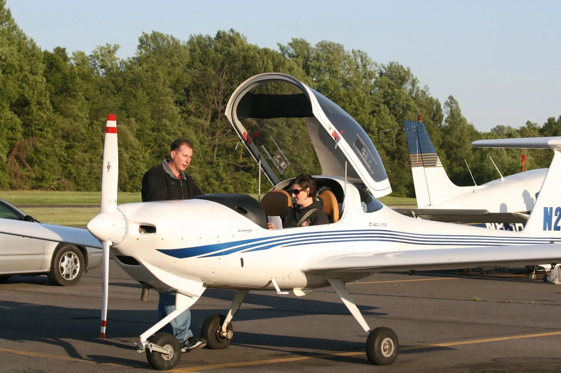 Man assisting a person in a small white plane with blue stripes, parked on a tarmac.