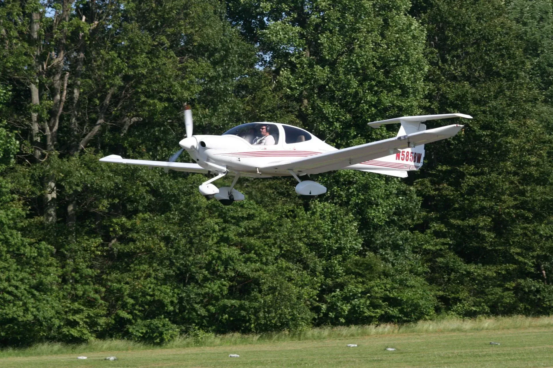 White airplane flying over a green grassy area near trees.