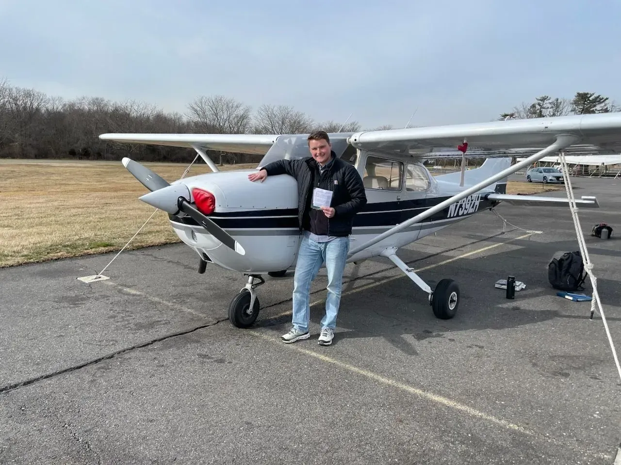 Man standing by small airplane on tarmac; overcast day.