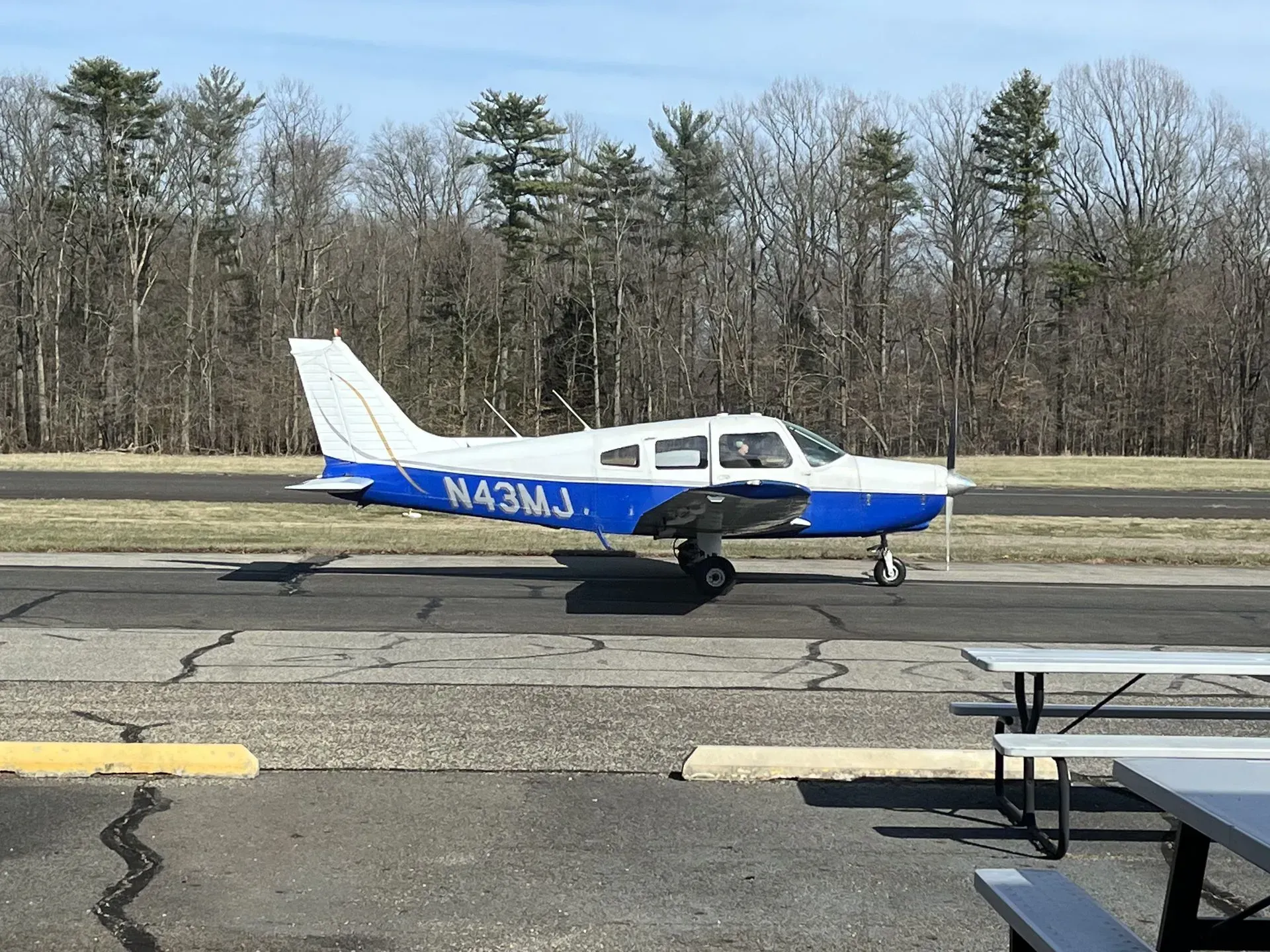 A blue and white airplane taxiing on a runway. Trees in the background.