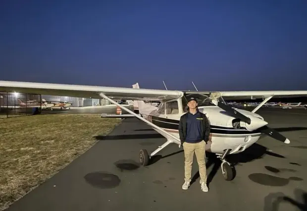 Person standing in front of a small airplane on a tarmac at dusk.
