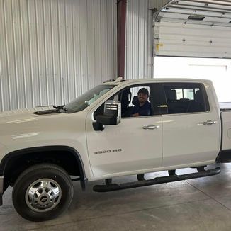 White pickup truck with a person in the driver’s seat, inside a garage-like building.