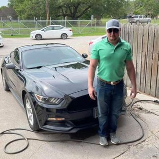 Man in green shirt and jeans stands next to a black Mustang.