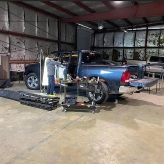 A person working on a blue pickup truck inside a garage with tools and equipment.