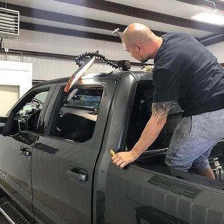 Man uses a dent puller on a gray truck in a workshop.