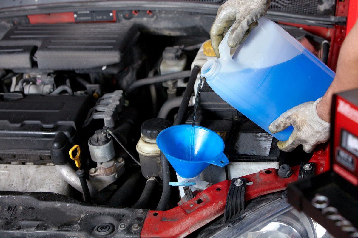 Person pouring blue liquid into a car engine with a funnel.