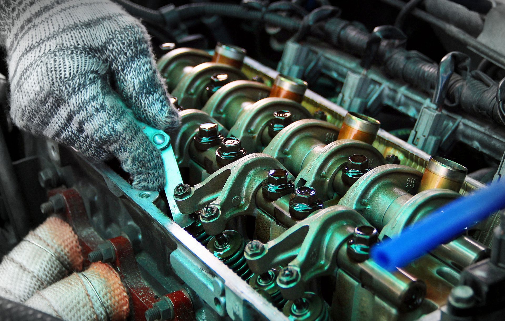Mechanic's gloved hand adjusting engine valves with a wrench in an engine bay.