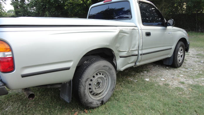 A white truck with a damaged side is parked in the grass.