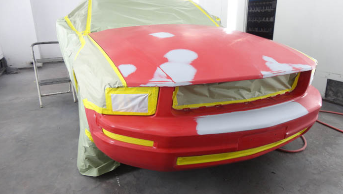 A red car is being painted in a garage.
