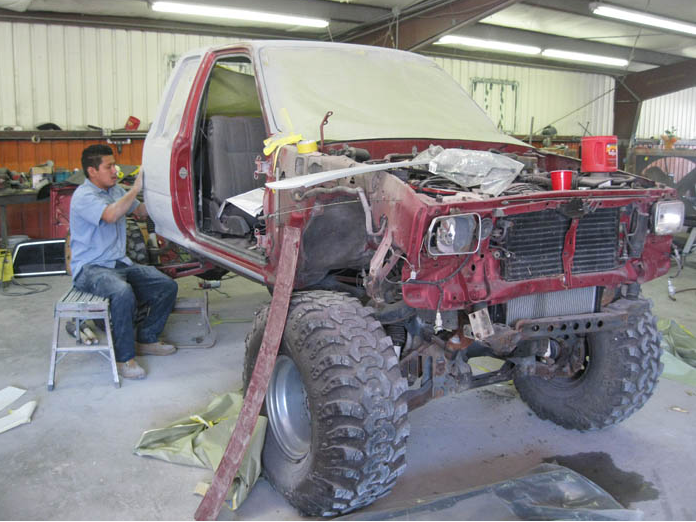 A man is sitting on a stool next to a red truck