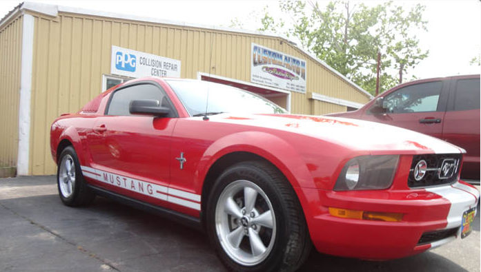 A red mustang is parked in front of a yellow building