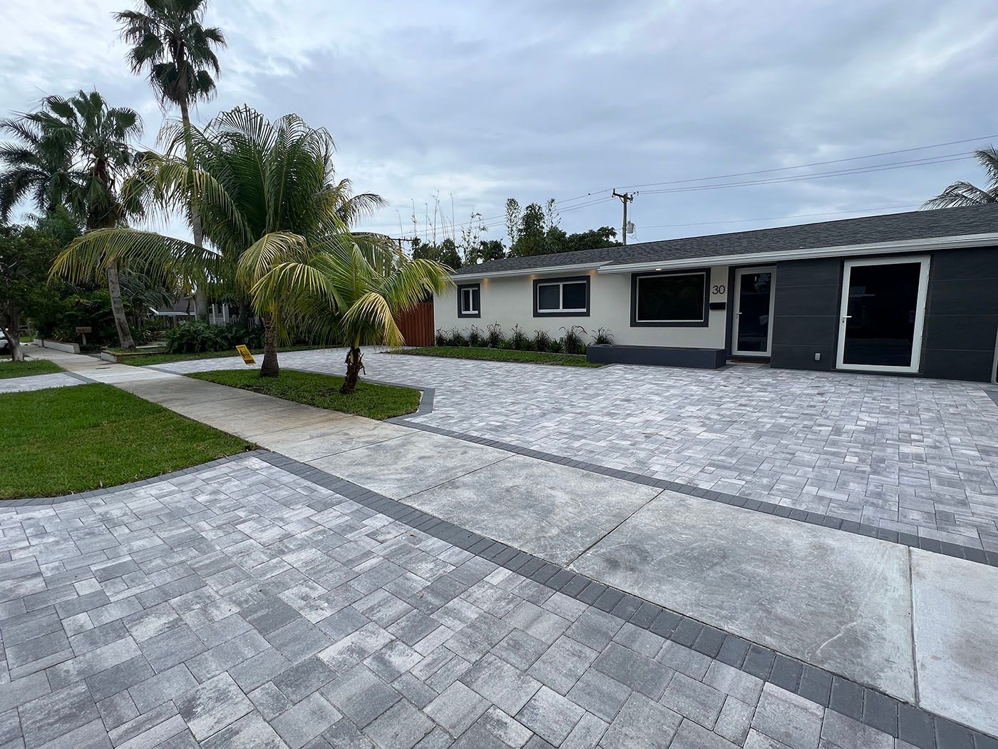 A house with a brick driveway and palm trees in front of it