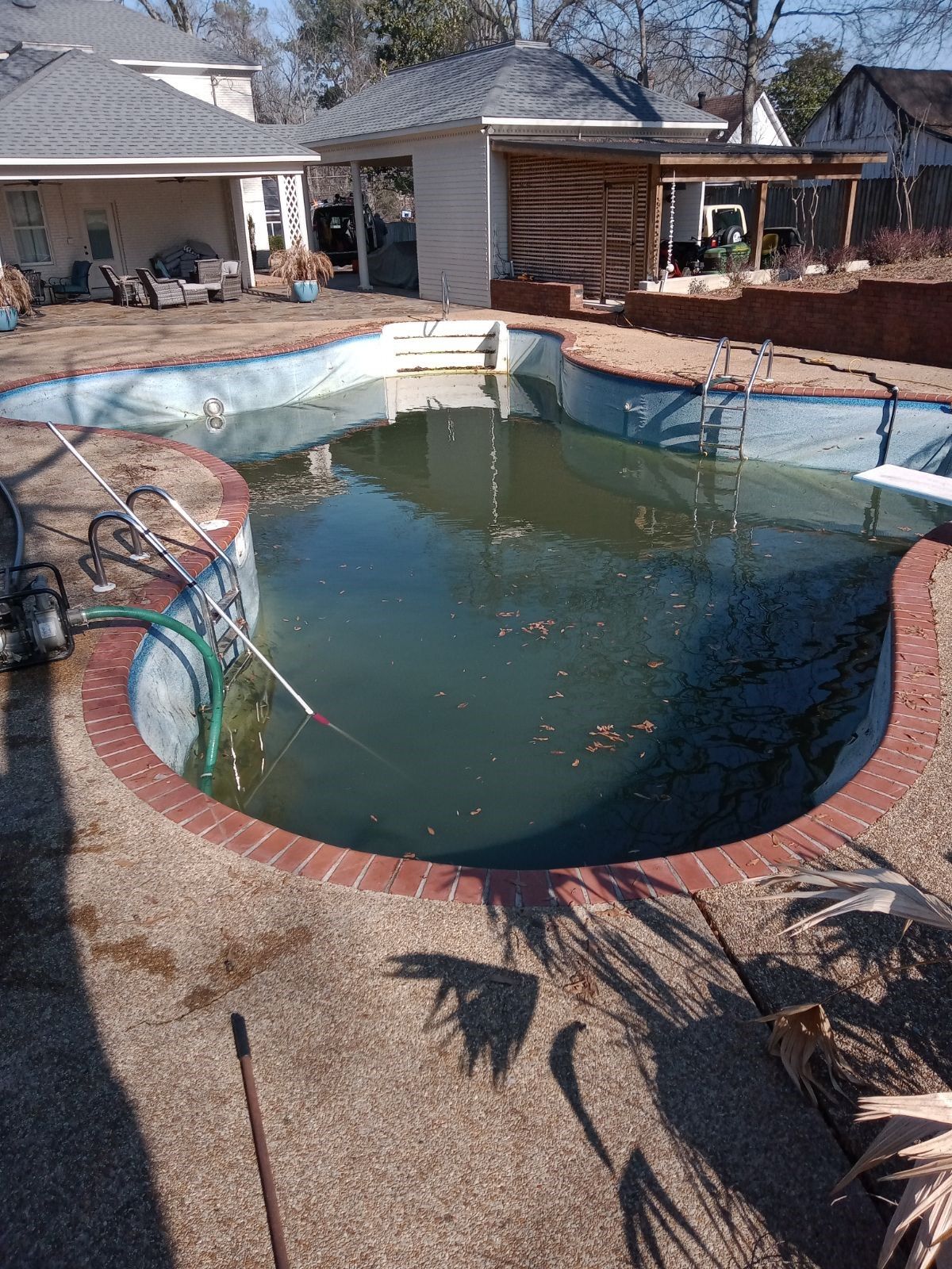 An empty swimming pool is sitting in the backyard of a house.