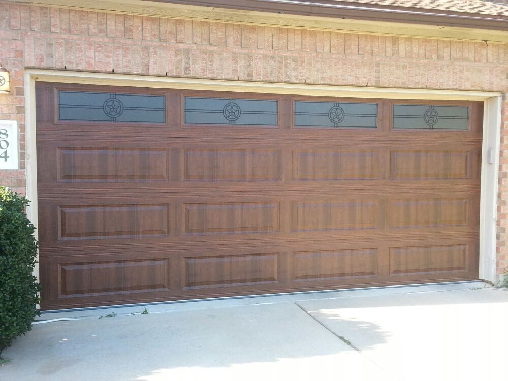 A wooden garage door with stained glass windows is sitting in front of a brick house.