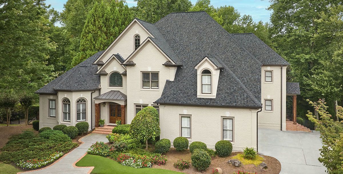 A large white house with a black roof is surrounded by trees.