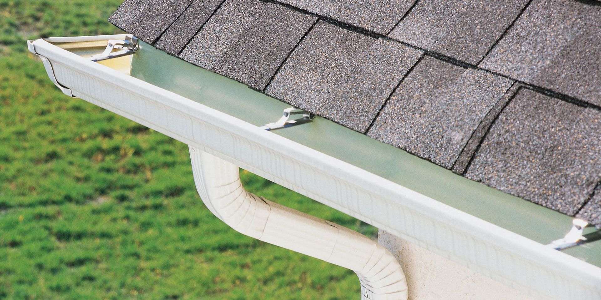 A white gutter is attached to the roof of a house.