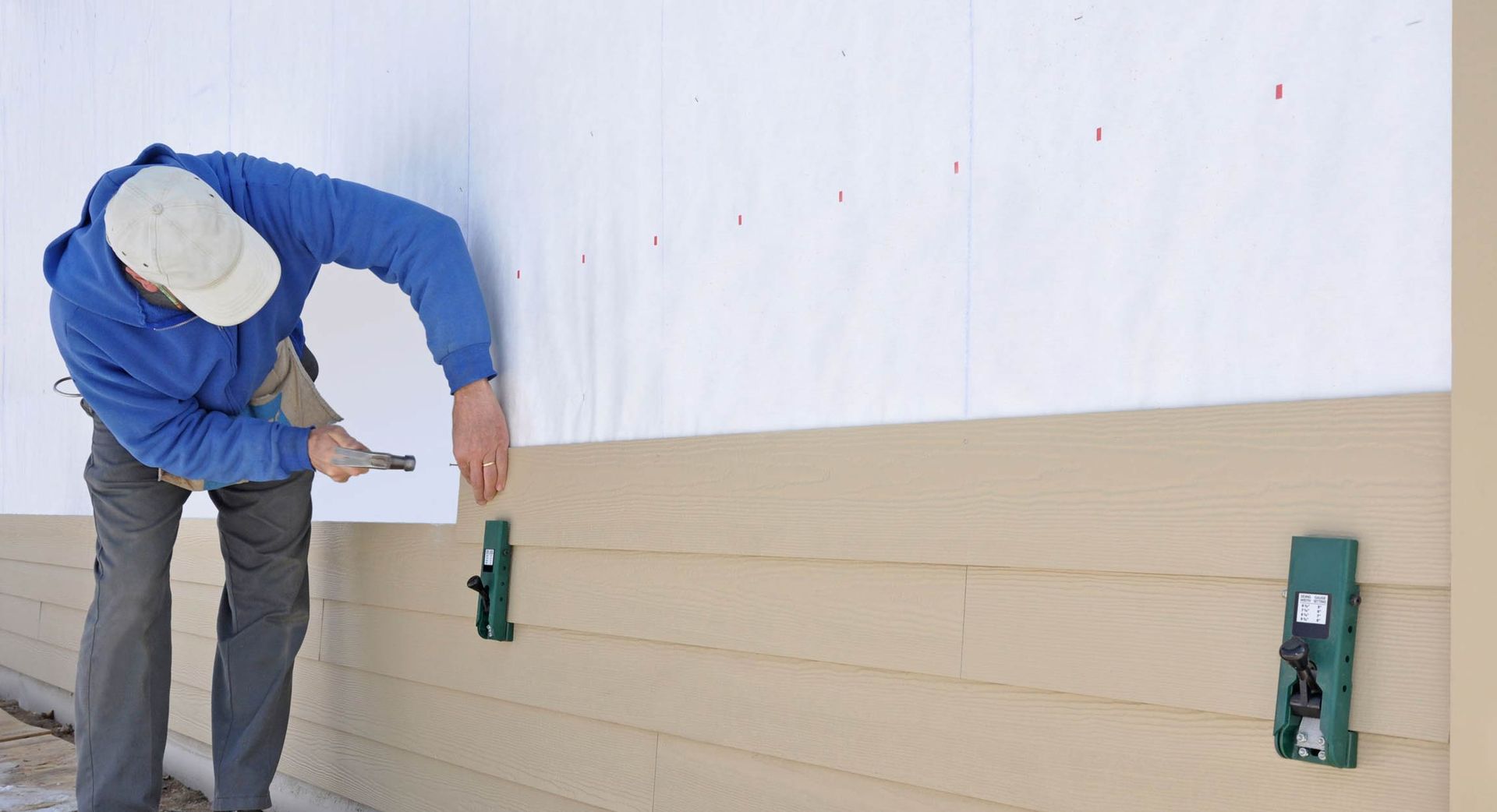 A man is installing siding on the side of a house.