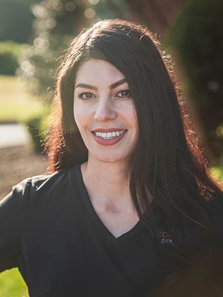 Woman with dark hair smiles outside, wearing a black top.