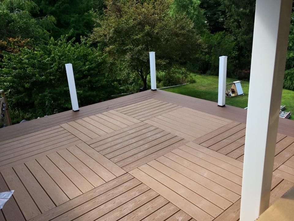 A wooden deck with a white railing and trees in the background