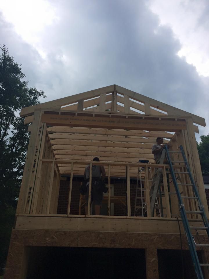 A man on a ladder is working on the roof of a house under construction.
