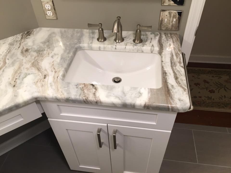 A bathroom sink with a marble counter top and white cabinets