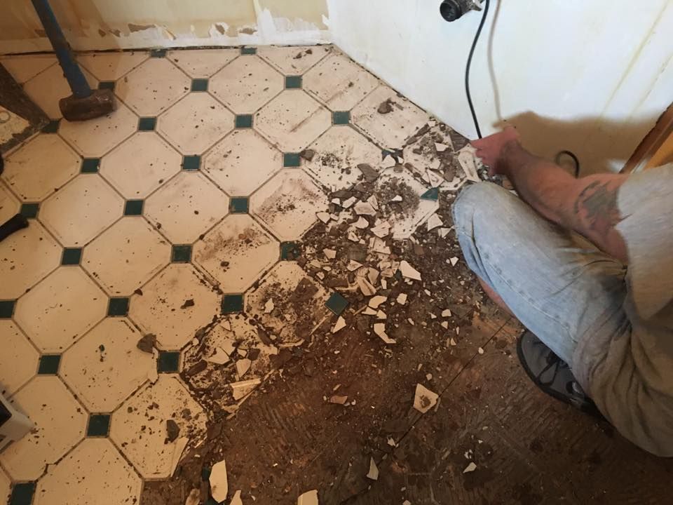 A person is kneeling on a tiled floor with a hammer.