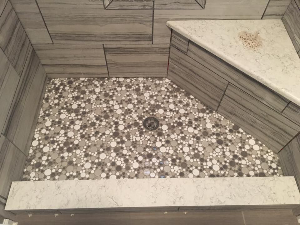 A shower stall with a mosaic tile floor and a bench.