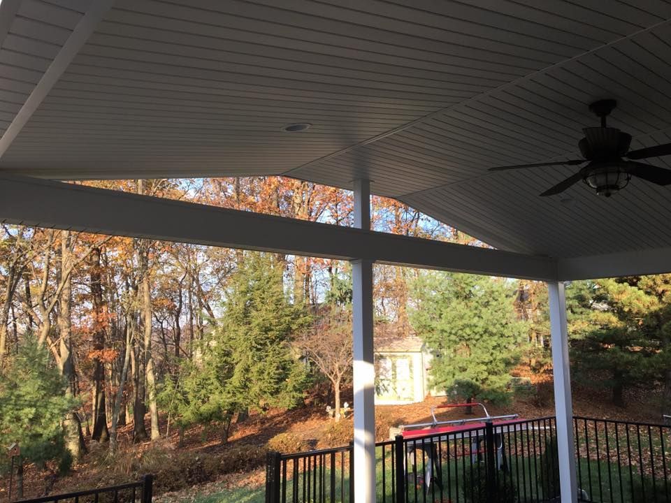 A porch with a ceiling fan and a view of a forest.