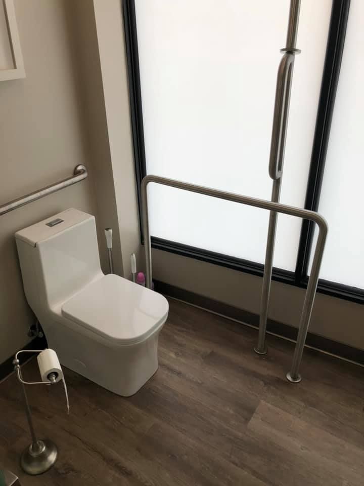 A toilet in a bathroom with a railing and a window.