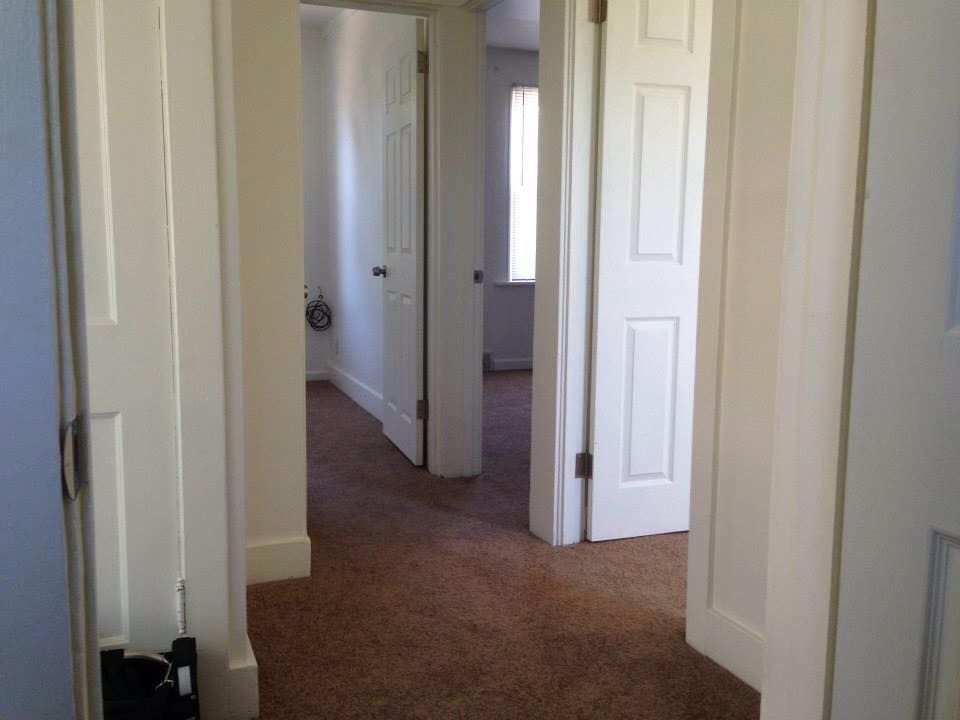 A hallway in a house with white doors and brown carpet.
