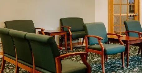 A waiting room with green chairs and tables