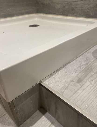 A white shower tray is sitting on top of a tiled floor in a bathroom.