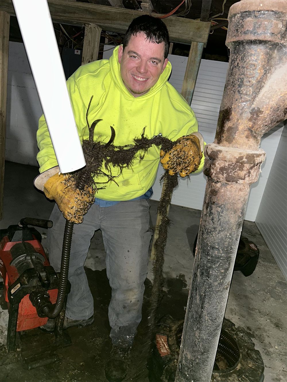A man in a yellow hoodie is holding a pipe and a hose.