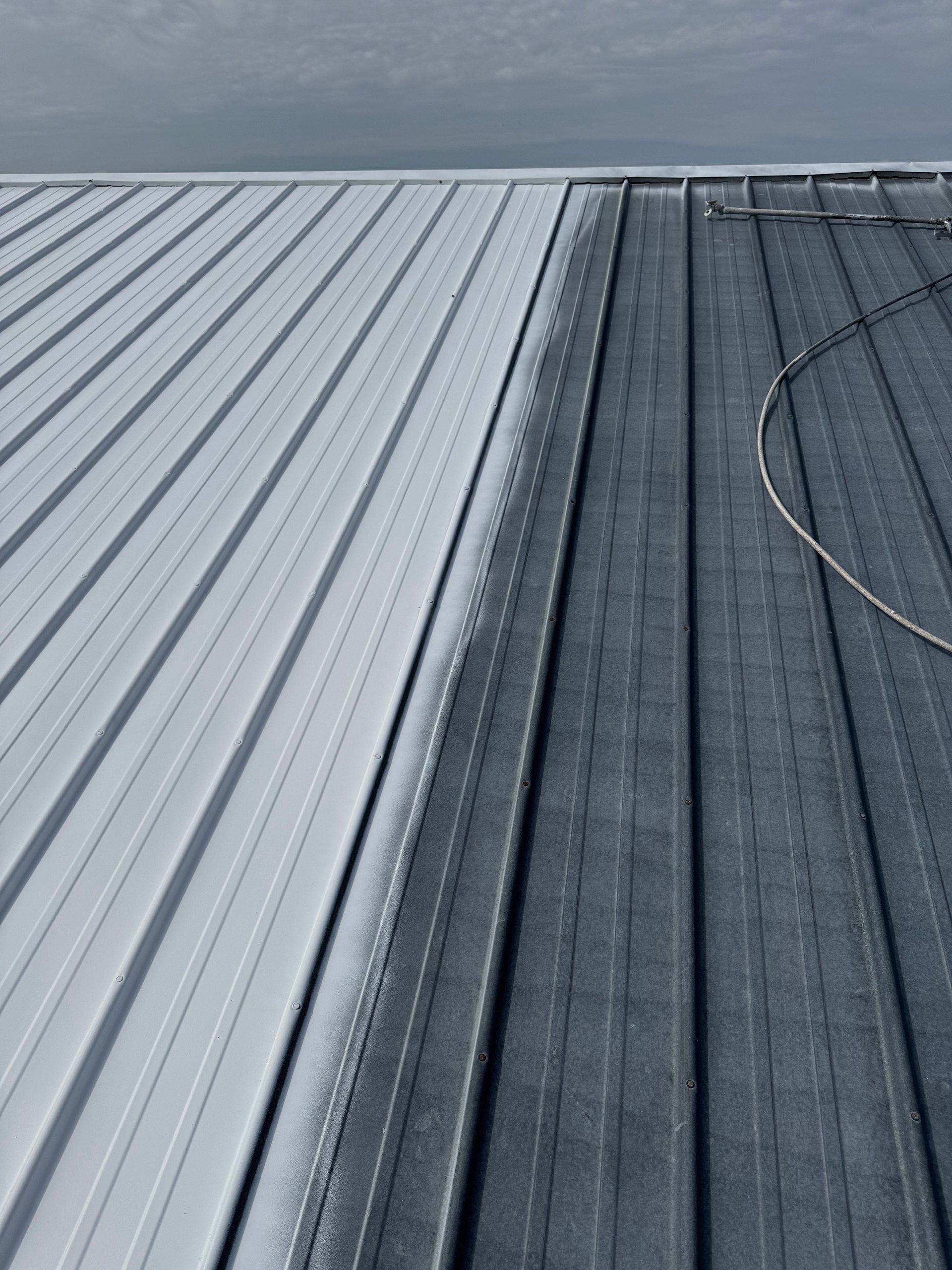 Close-up of light and dark corrugated metal roofing with a cable on the right side.