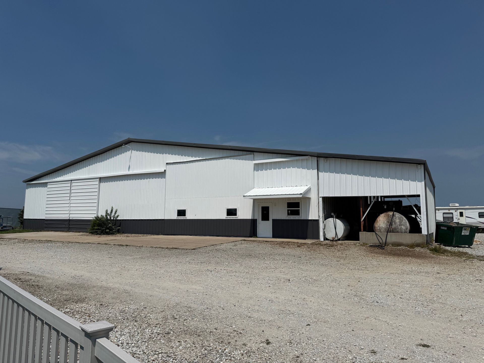 White agricultural barn with open bays on a gravel lot under a clear blue sky
