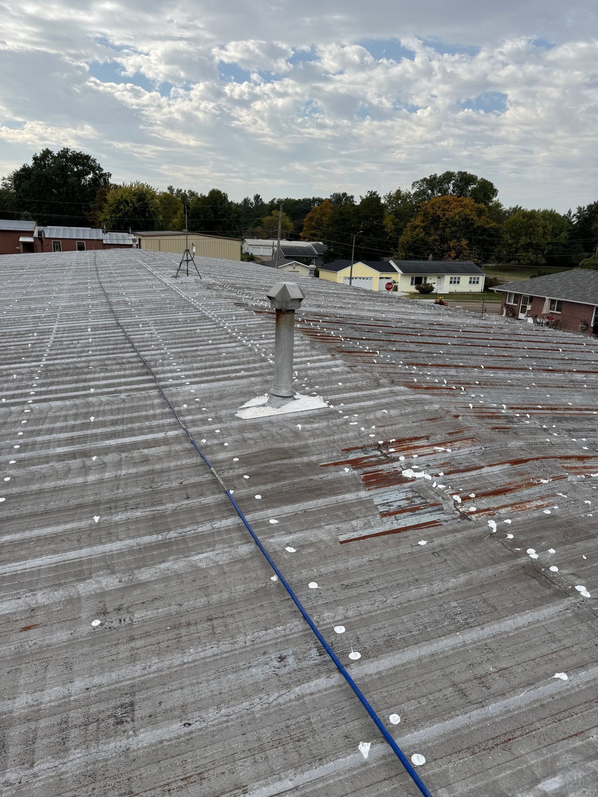 Rooftop covered in reflective material with a white vent pipe under a cloudy sky.