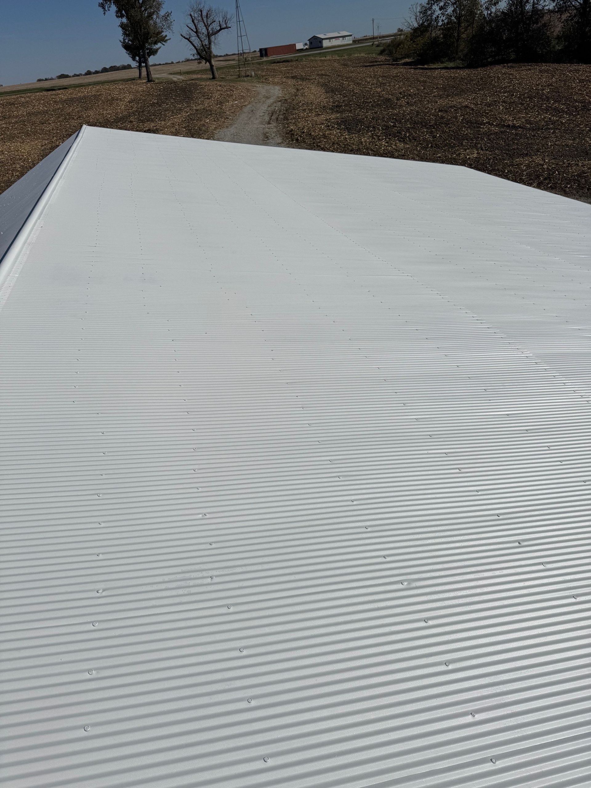 A bright white, textured surface with parallel grooves set against a rural landscape with trees under a blue sky.