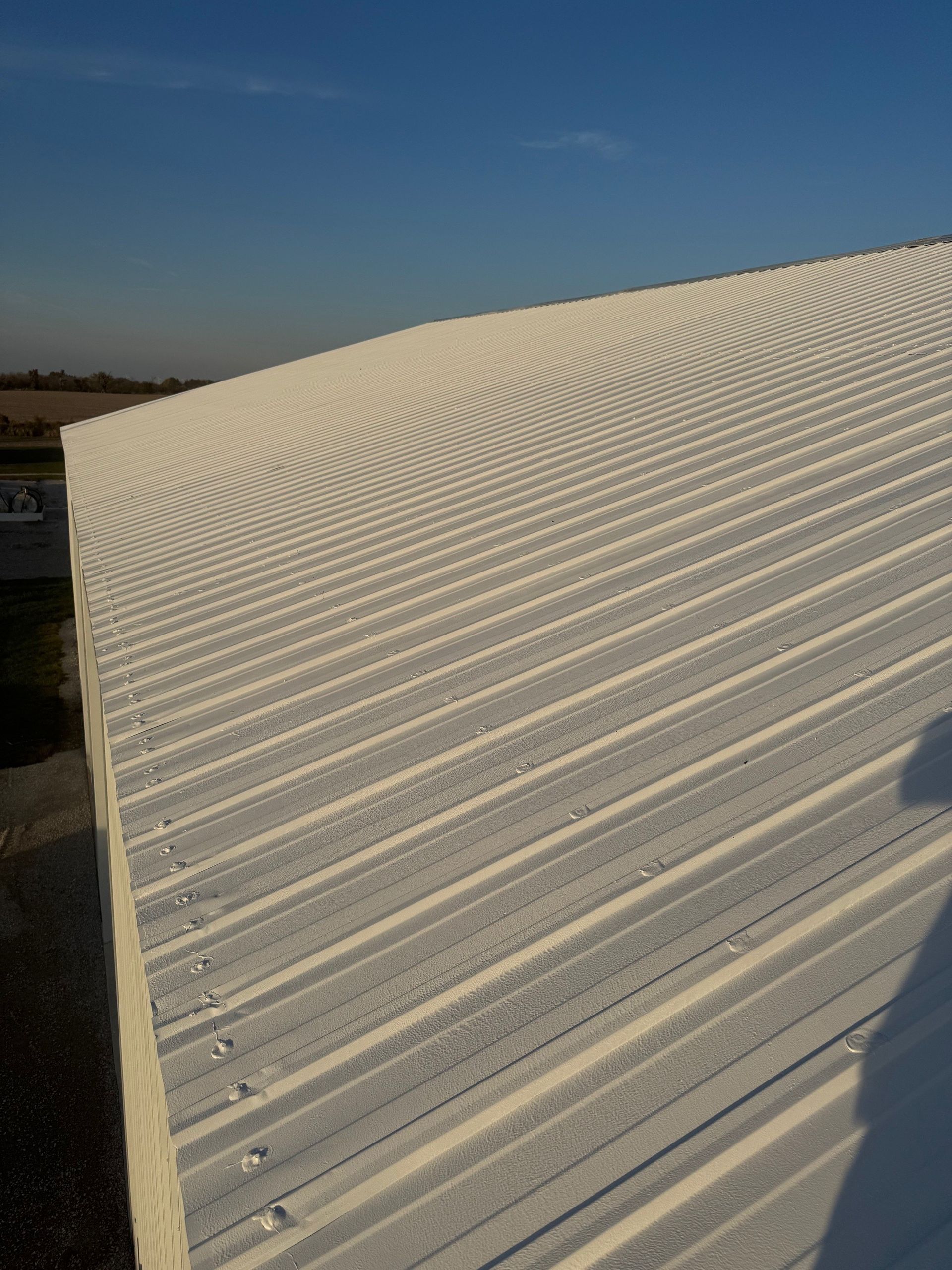 A high-angle view of a white, corrugated metal roof under a clear, bright blue sky.