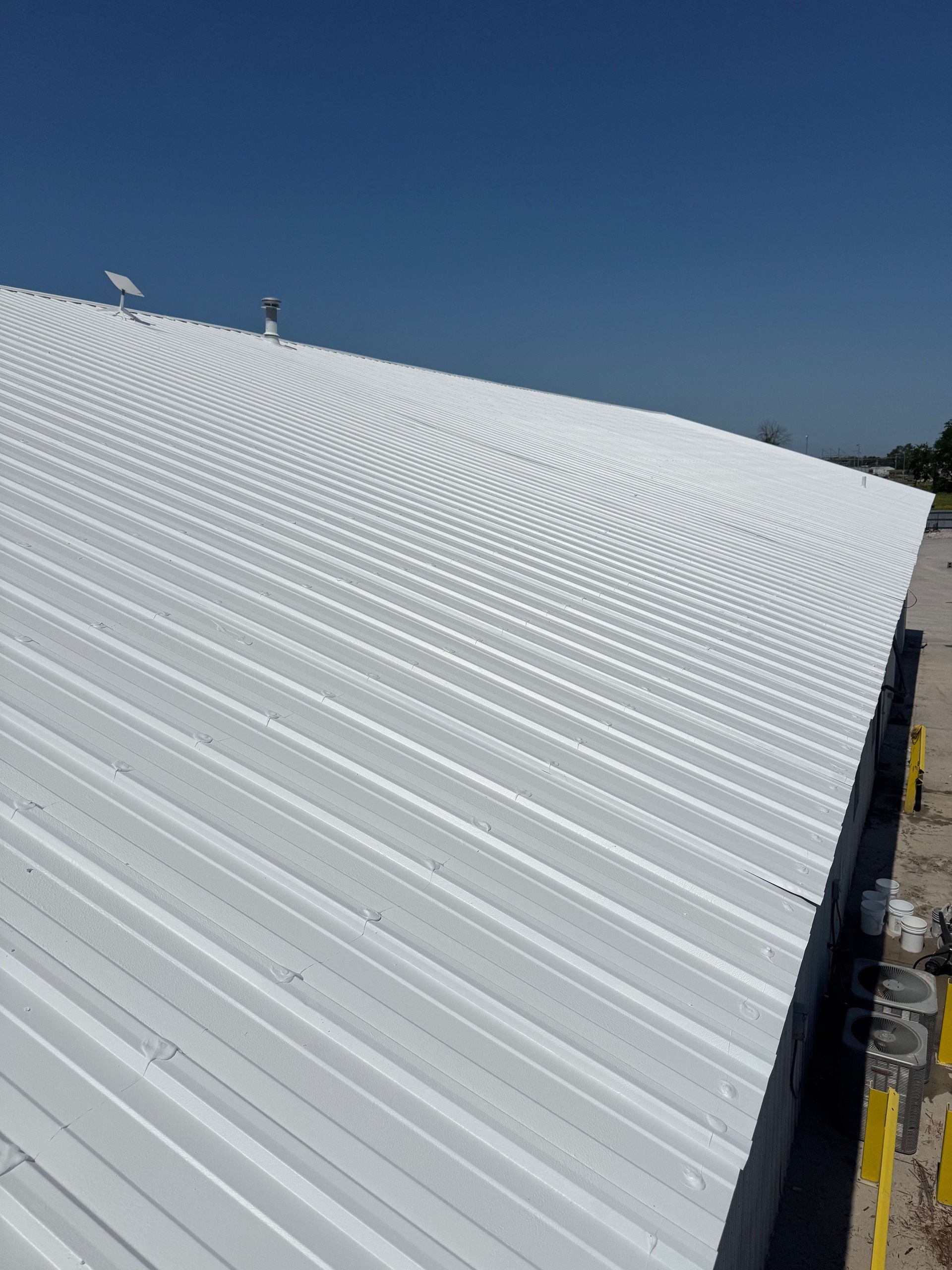 A high-angle view of a large white, corrugated metal roof under a bright blue sky.