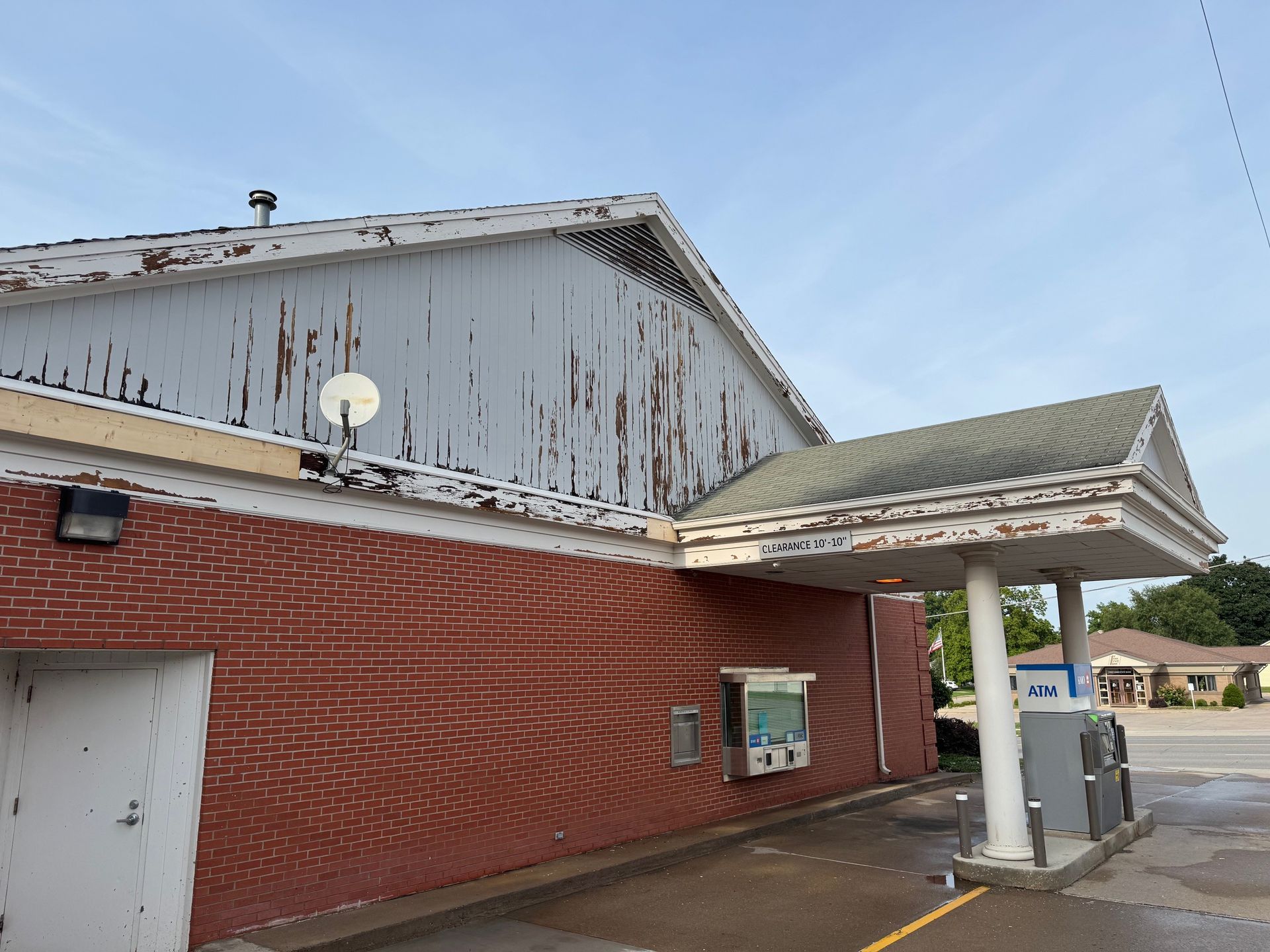 A brick building with a weathered, peeling facade and an attached drive-thru canopy, exterior day view.