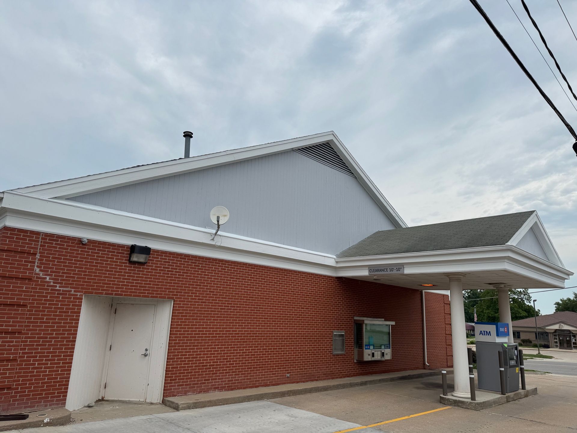A brick building with an ATM drive-thru lane and an exterior door under a cloudy sky.