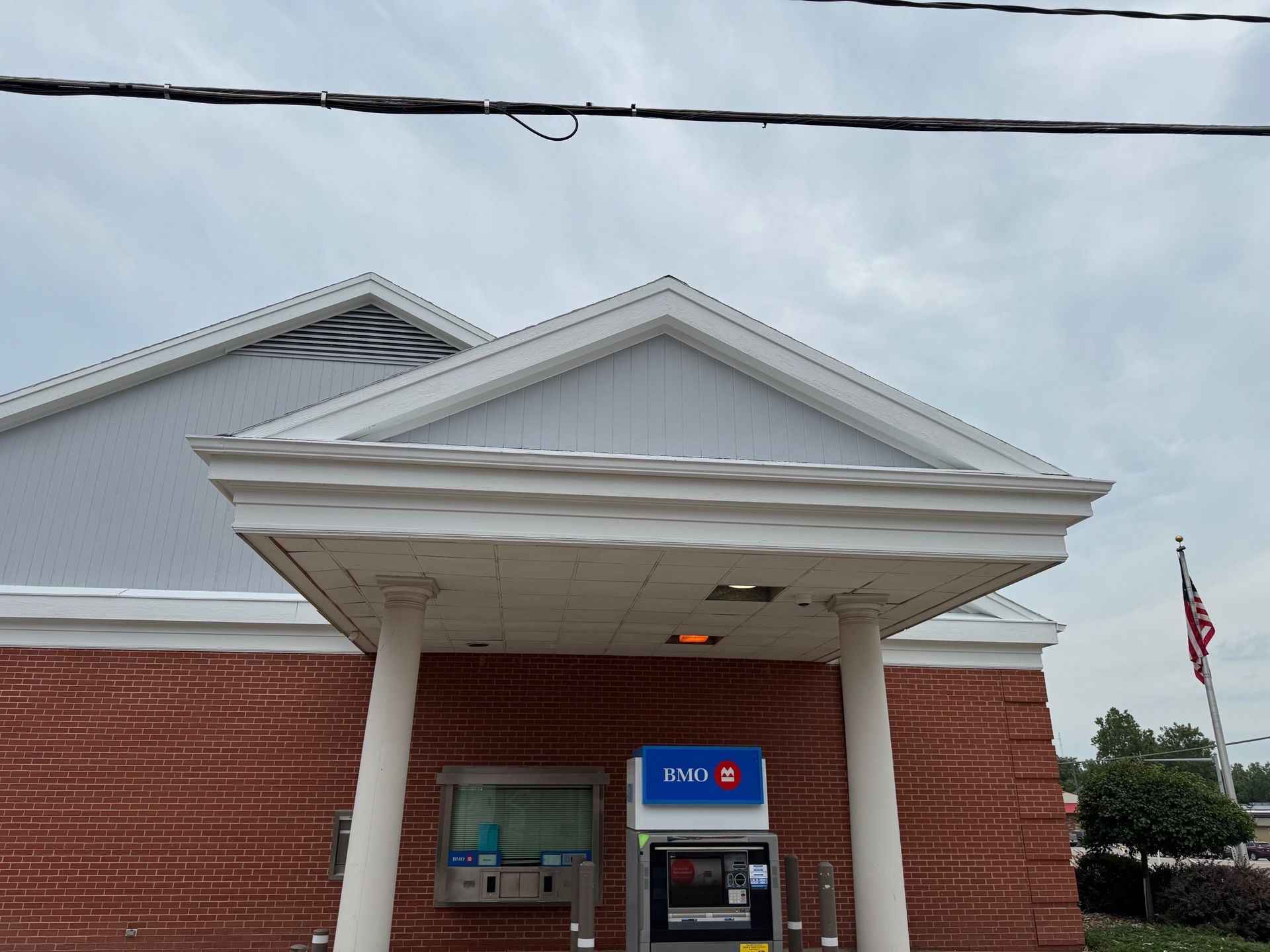 ATM machine located under a white awning of a brick building with a pediment roof against a cloudy sky.