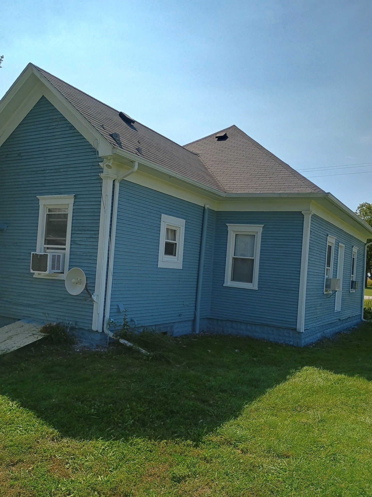 Blue house exterior with damaged roof shingles and bright green lawn in sunlight