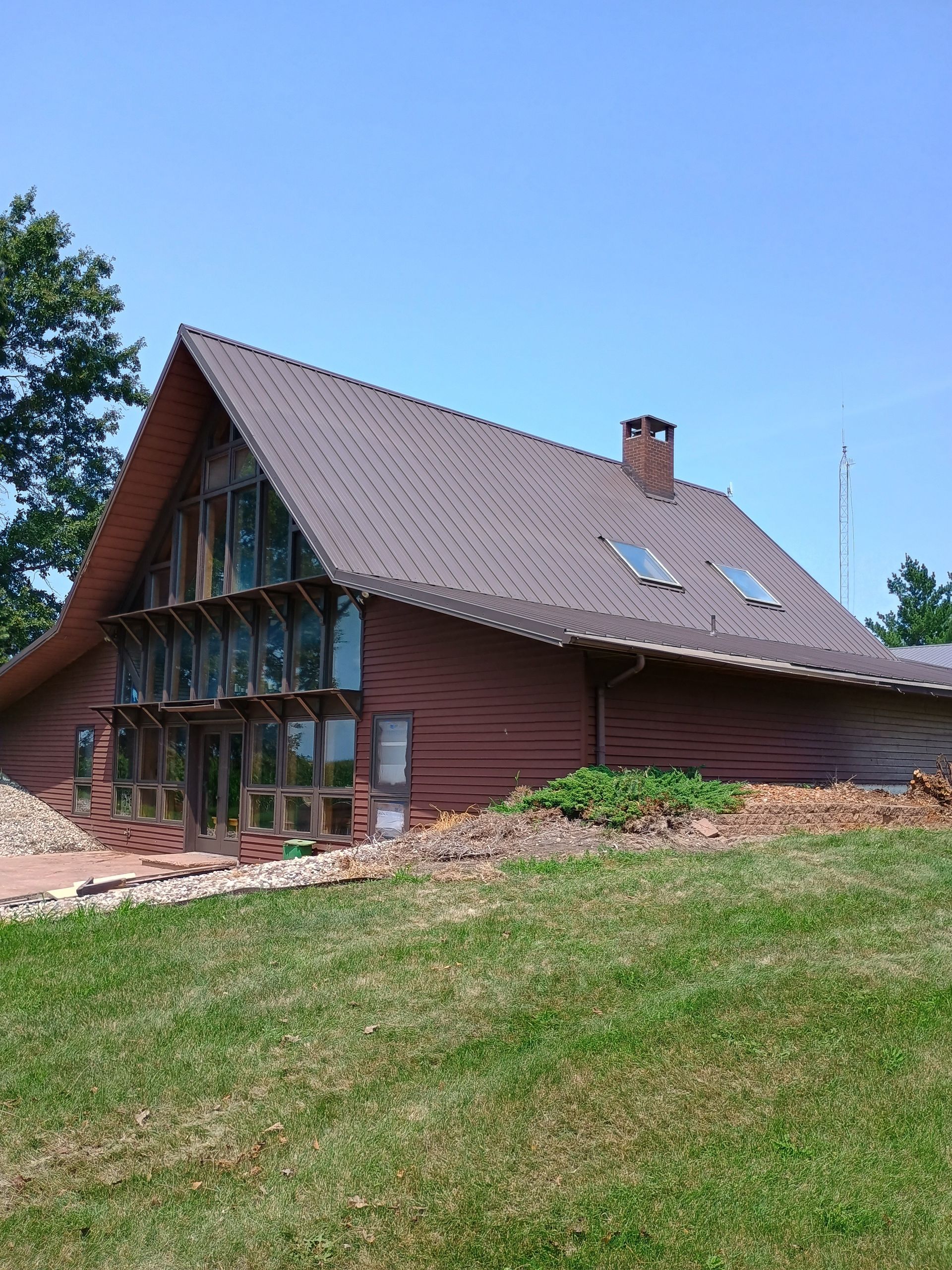 Red wooden house with a steep roof on a grassy hillside under a clear blue sky.