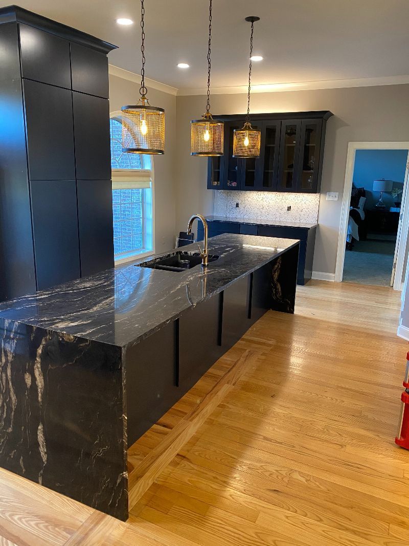 A kitchen with black cabinets, granite countertops, and hardwood floors.
