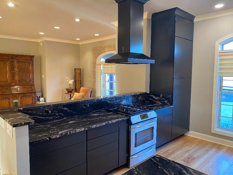 A kitchen with black cabinets, a stove, and a hood.