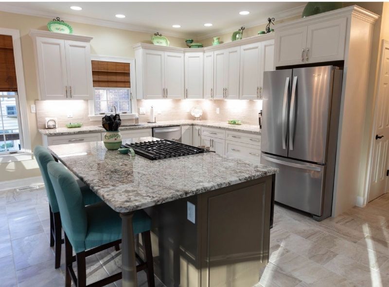 A kitchen with white cabinets, granite countertops, stainless steel appliances, and a large island.